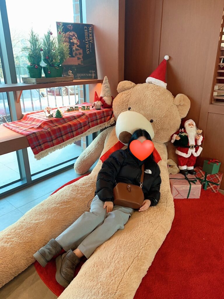 Wearing The North Face Retro Nuptse 1996 jacket sitting next to a giant teddy bear in a cafΓ©.