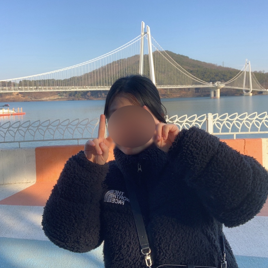 Wearing The North Face Sherpa Nuptse Jacket while posing playfully with hands near a riverside bridge.