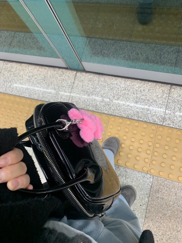 enamel comme des garcons aoyama bag with pink charm on subway platform