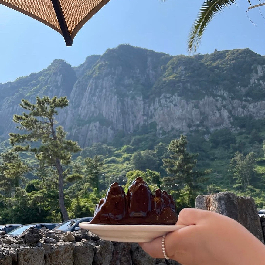 Panoramic view of One and Only Jeju CafΓ© with Sanbangsan mountain and ocean scenery