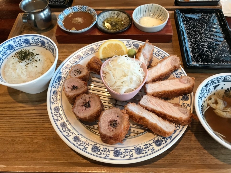 Full Jeju black pork cutlet meal with sauces, rice, and soup served on a wooden table