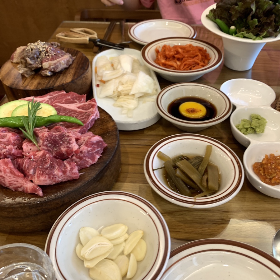 Korean BBQ beef assortment with marinated cuts, garlic, and side dishes on wooden table