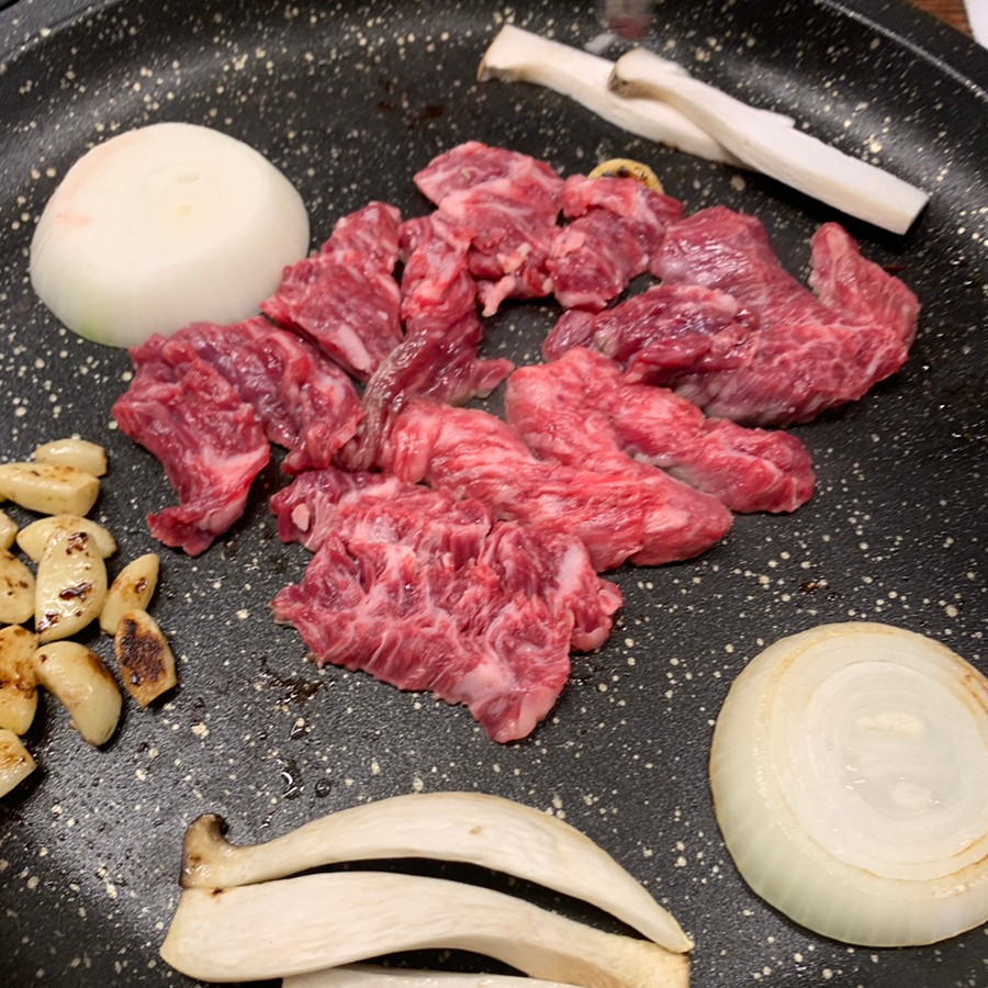 Fresh marbled beef grilling with garlic, onion, and mushrooms on a Korean BBQ grill